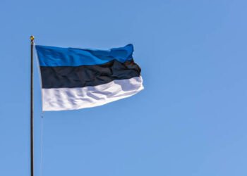 Estonian flag on the flagpole, waving in the wind against a blue sky.